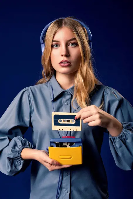 Young blond woman with walkman and headphones in front of blue background