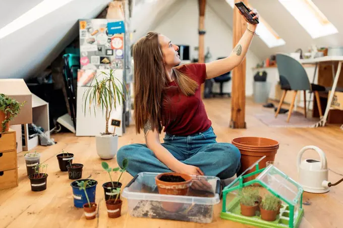 Young woman taking selfie with plants on wooden floor