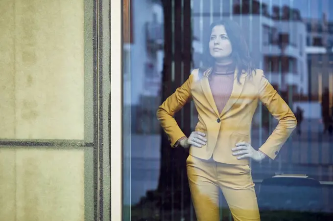 Confident businesswoman wearing yellow suit standing behind windowpane