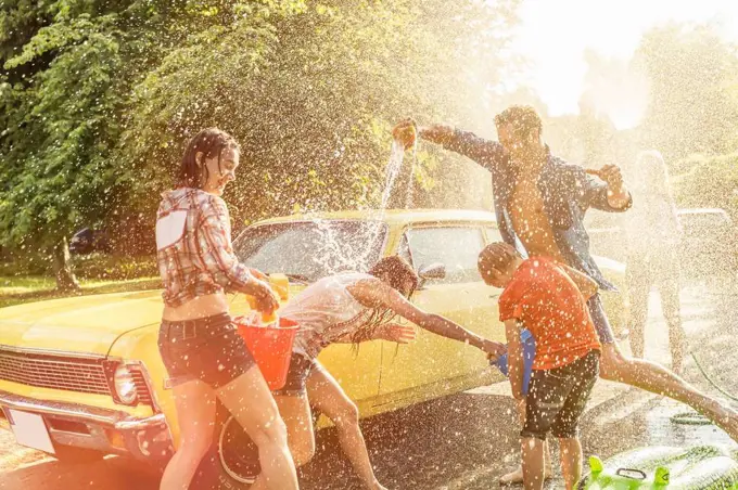 Group of friends washing yellow vintage car in summer having fun