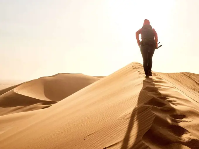 Woman walking on the ridge of a dune in the desert, Walvis Bay, Namibia