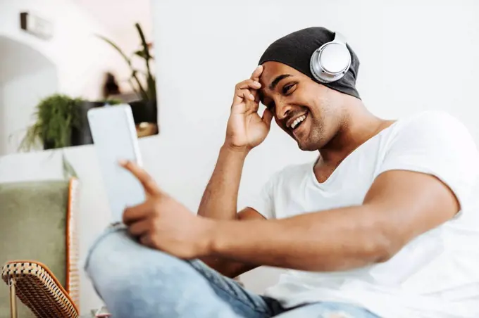 Portrait of smiling man using mini tablet and headphones at home