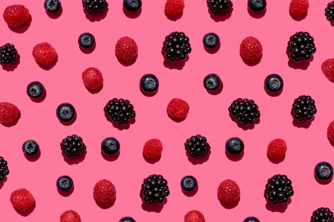 Pattern of raspberries, blueberries and blackberries against pink background