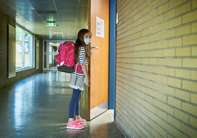 Girl wearing mask in school opening classroom door