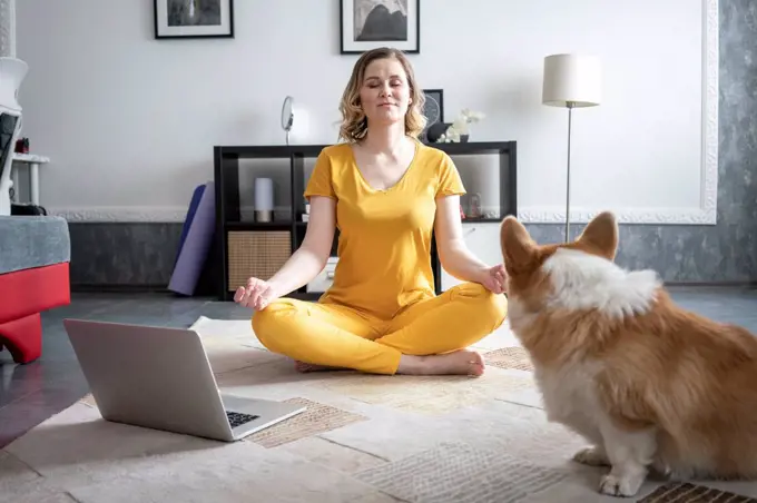 Woman with dog practising yoga in living room at home