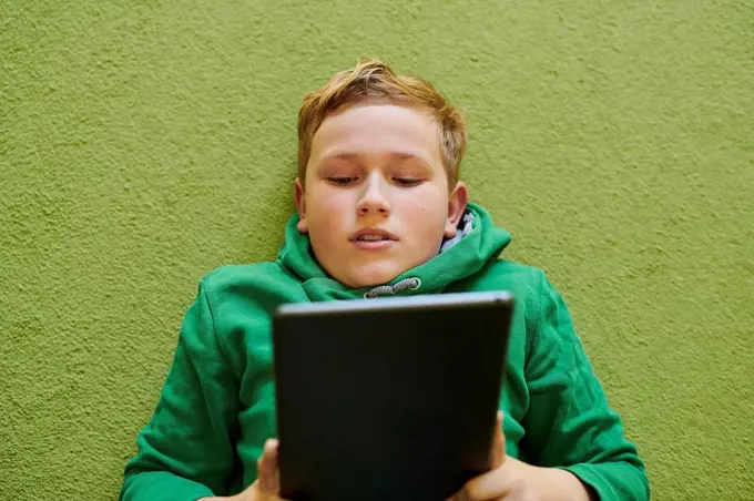 Boy using digital tablet on green carpet at home
