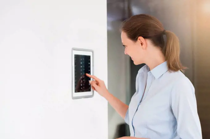 Mid adult woman using digital lightning control on wall at home