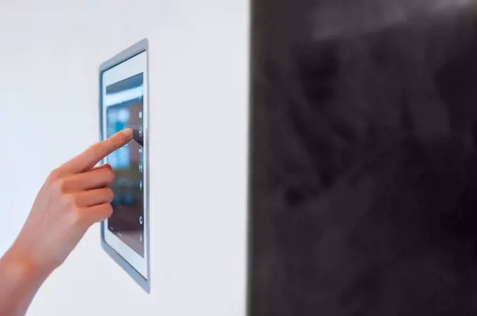 Hand of woman using digital lightning control mounted on wall at home