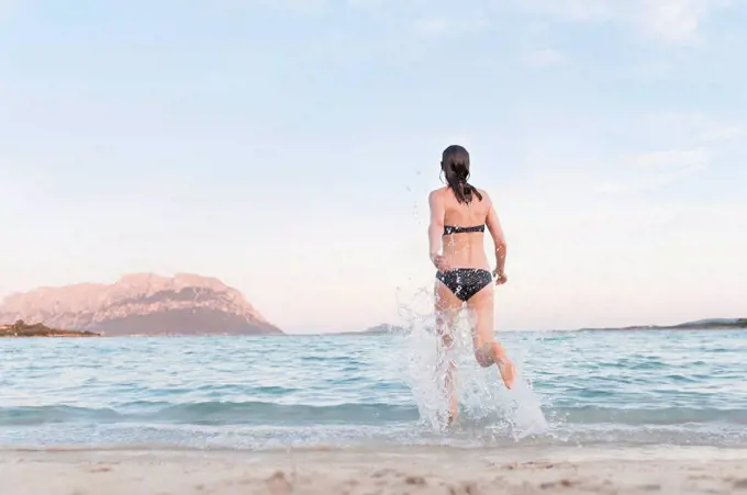 Back view of woman in bikini running into the sea, Sardinia, Italy