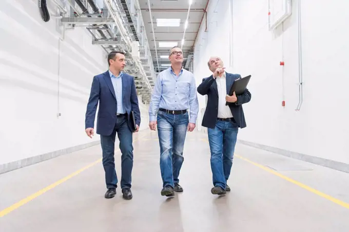Three businessmen walking and talking on factory corridor