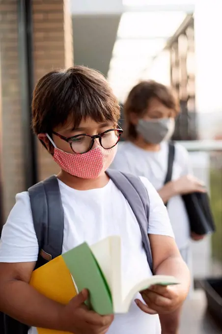 Siblings wearing masks outdoors, boy reading book