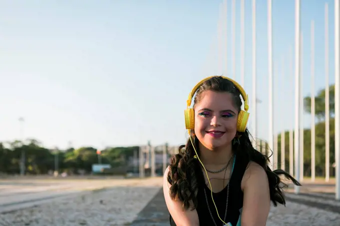 Teenager girl with down syndrome wearing 8s colorful makeup and listening to music with yellow headphones