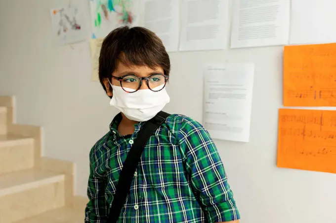 Boy wearing mask looking away while standing against wall in school