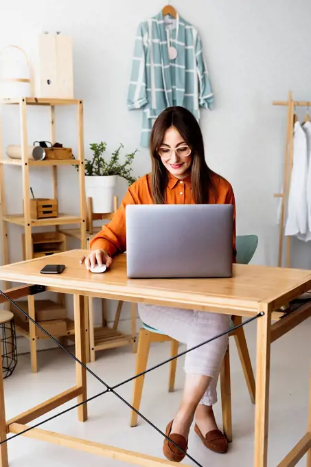 Female fashion designer working at home sitting at desk with laptop