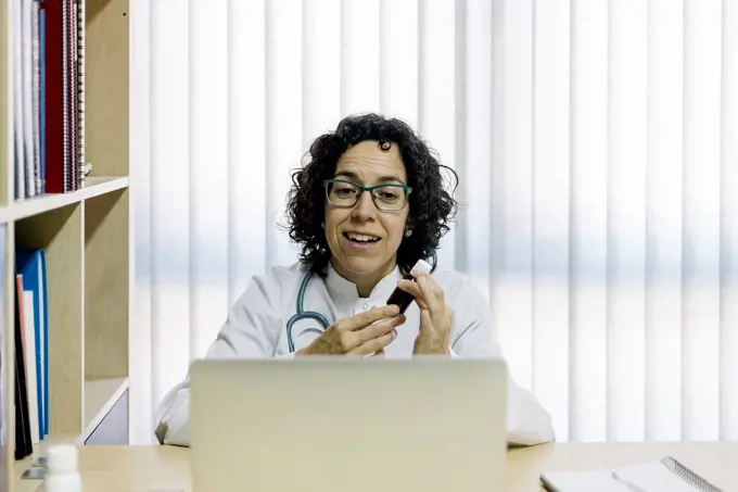Smiling female doctor discussing medicine through video call on laptop in office