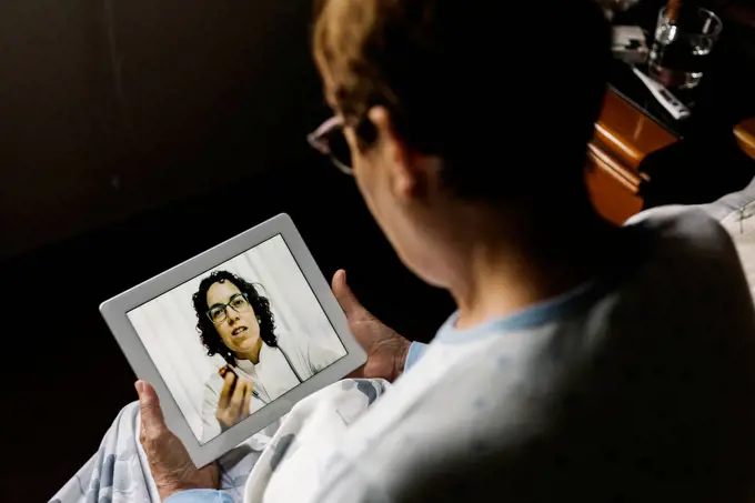 Elderly woman discussing over video call through digital tablet with doctor in bedroom