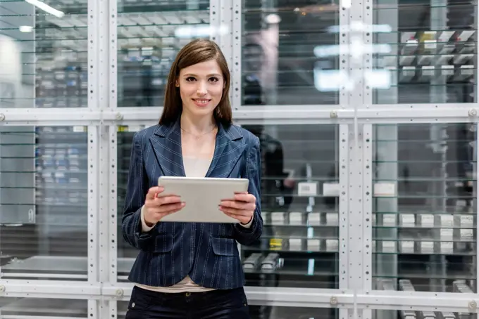 Smiling businesswoman using digital tablet while standing against glass in factory