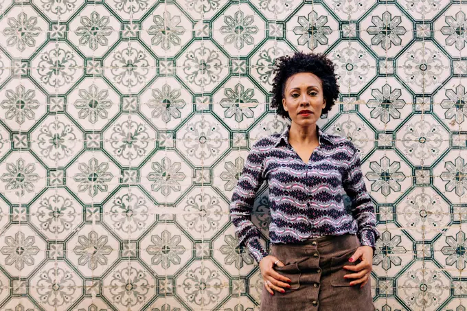 Stylish mid adult woman with curly hair standing against tiled wall