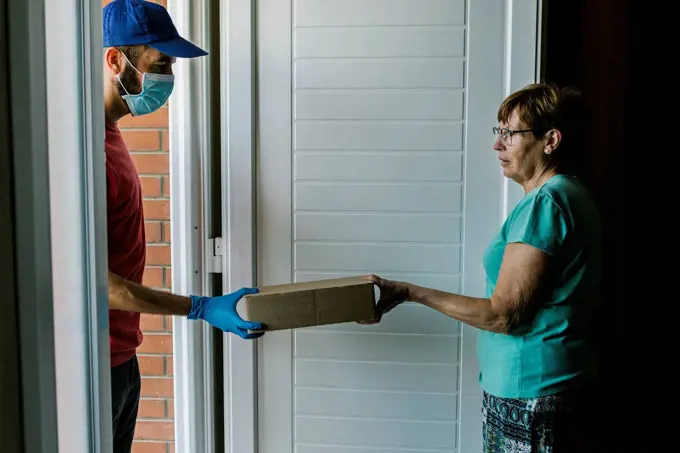 Postal worker delivering package to senior woman at doorway during coronavirus