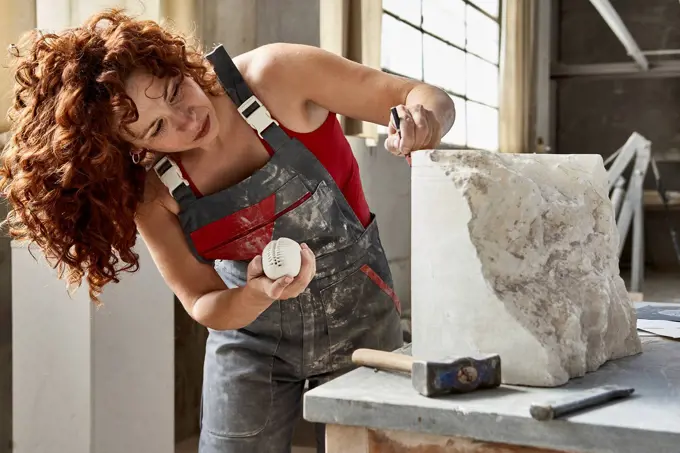Female stonemason in overalls measuring stone on table at workshop