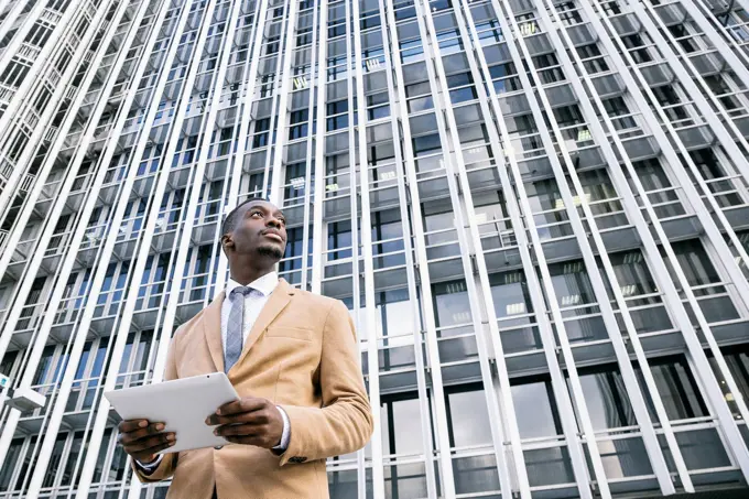 Young businessman in front of modern office building in the city holding a tablet