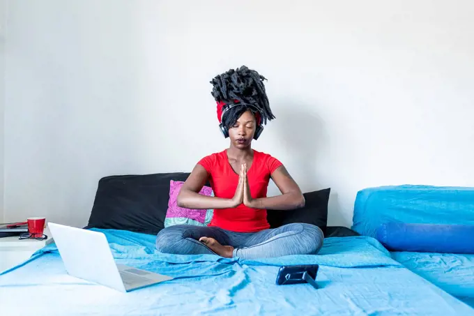 Young woman meditating at laptop sitting on bed