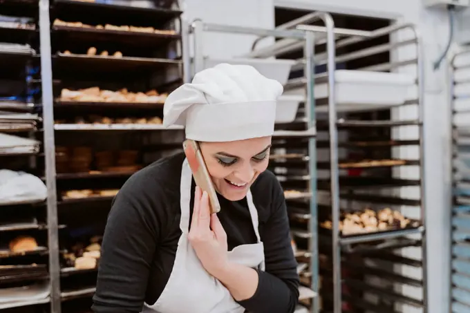 Happy female baker using smart phone in kitchen at bakery