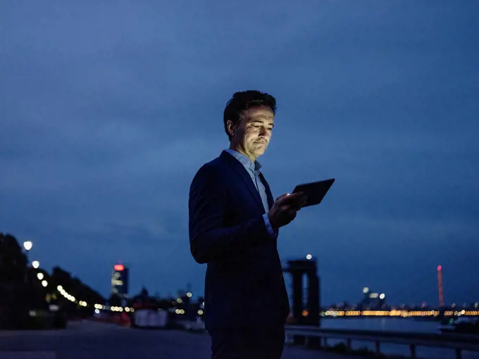 Mature businessman using tablet at the riverbank at dusk