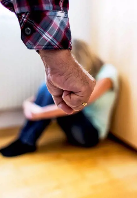 Man's fist in front of a young woman crouching afraid on the floor