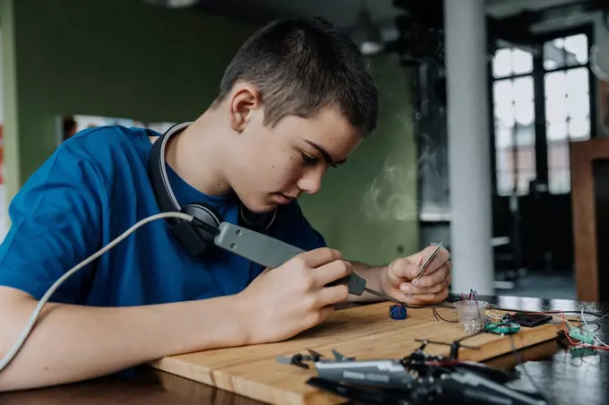 Boy sitting at home using soldering iron