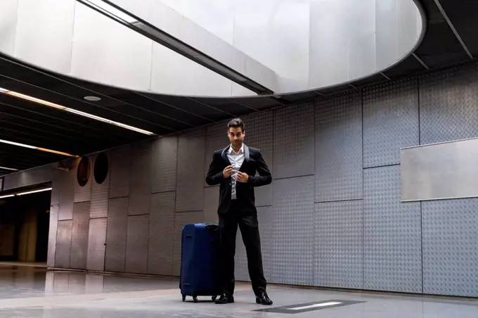 Businessman with wheeled luggage standing on floor at station