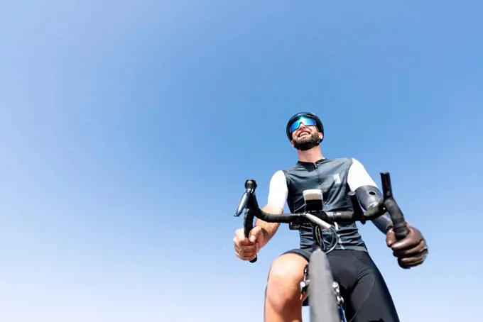 Male amputee cyclist with artificial limb riding bicycle against clear sky