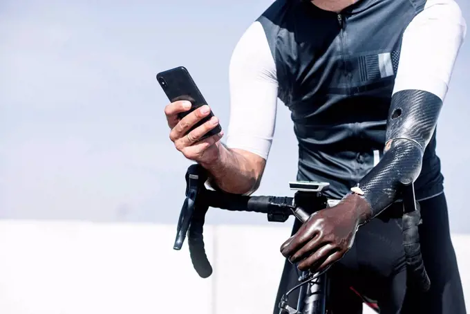 Close-up of amputee athlete using smart phone while standing with bicycle