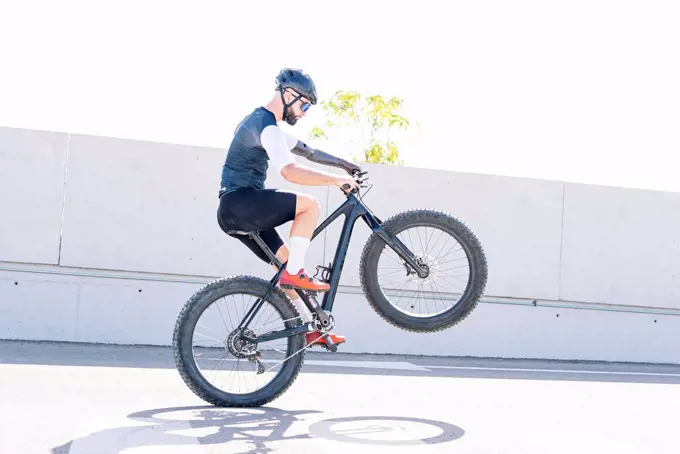 Male amputee athlete performing stunt with bicycle on road against clear sky