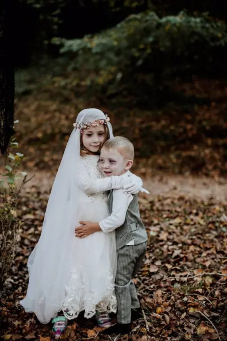 Sister embracing brother at halloween party while standing in forest