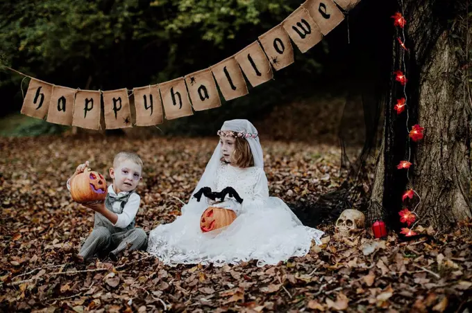 Sibling playing with halloween toy while sitting in forest