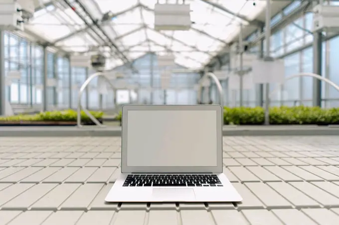 Laptop on floor with plants in background at greenhouse
