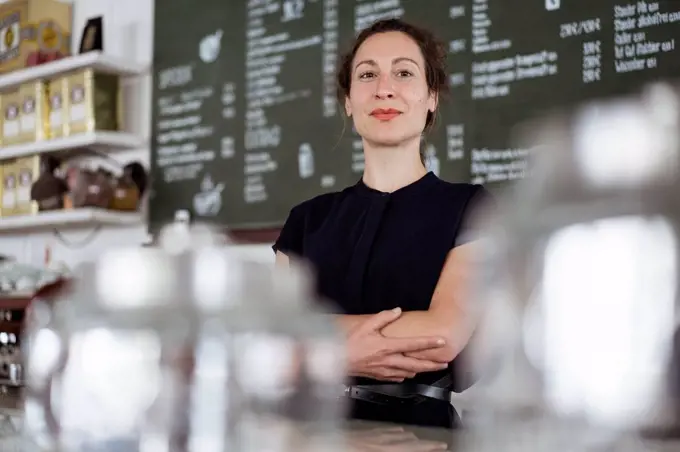 Confident female owner standing against blackboard in coffee shop