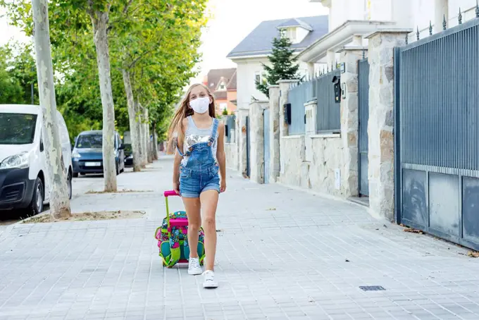 Girl with schoolbag walking on footpath wearing protective face mask