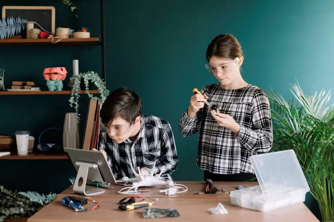 Siblings using digital tablet while preparing drone on table against wall at home