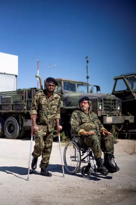 Injured military officer holding crutches while standing with disabled army soldier on wheelchair during sunny day