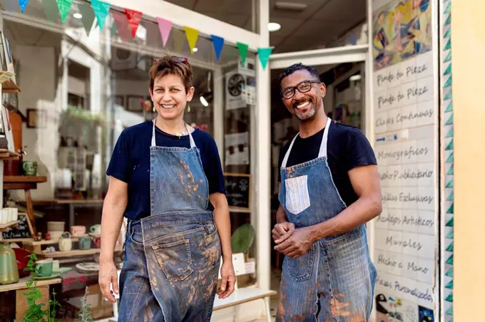 Smiling coworkers wearing aprons standing outside ceramic shop