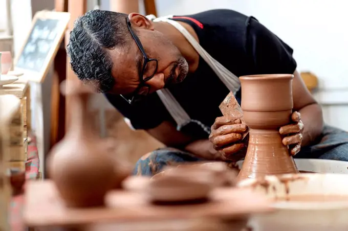 Close-up of male artist making earthenware on pottery wheel in workshop