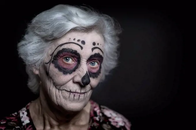 Portrait of senior woman with sugar skull make-up in front of black background