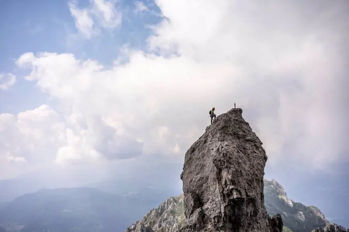Male hiker standing on top of mountain against cloudy sky, European Alps, Lecco, Italy
