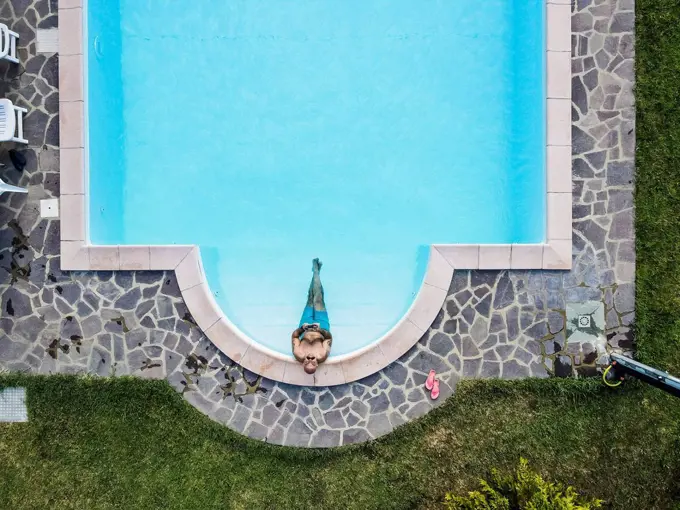 Drone view of man relaxing swimming pool