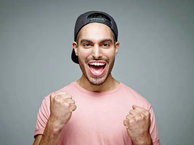 Portrait of man with baseball cap screaming for joy in front of grey background