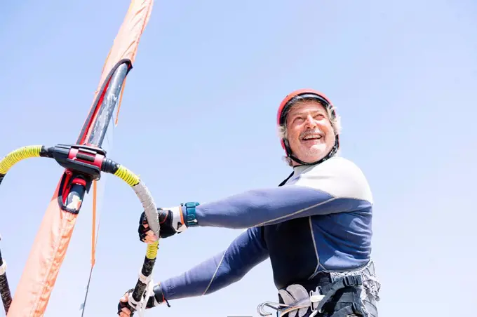 Cheerful senior man windsurfing against clear sky during sunny day