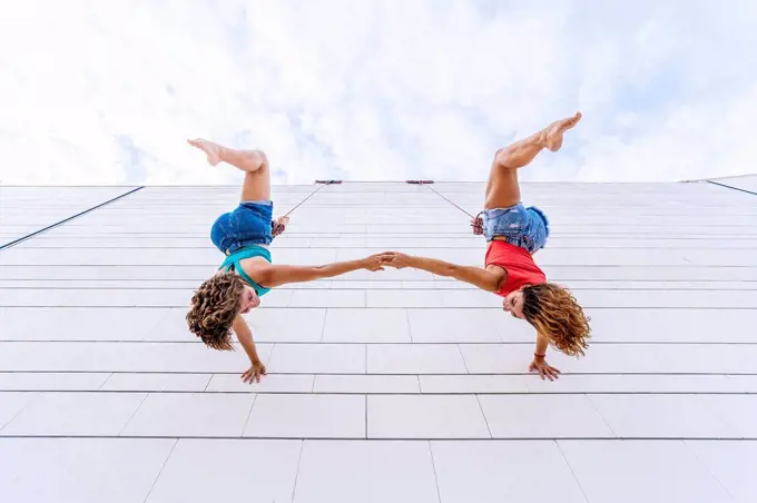 Aerial dancers upside down holding hands while hanging on window