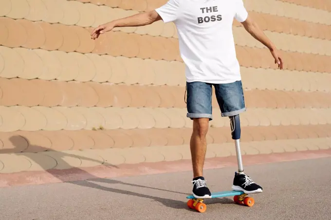 Young man with artificial limb and foot standing on skateboard at sports court